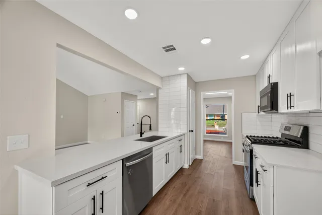 a large white kitchen with a lot of counter space and wooden floor