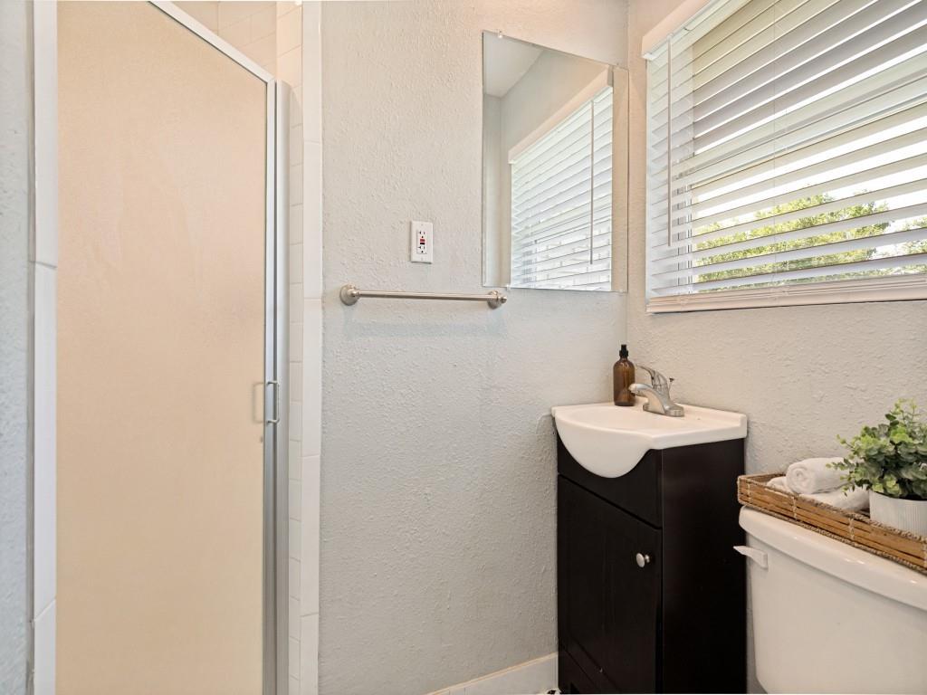 1405 Rambler Road Arlington, TX 76014 - Photo 19 of 26 Corner vanity with integrated sink, shower enclosure with frosted glass, wall-mounted mirror, and horizontal window blinds