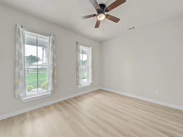 an empty room with wooden floor fan and windows