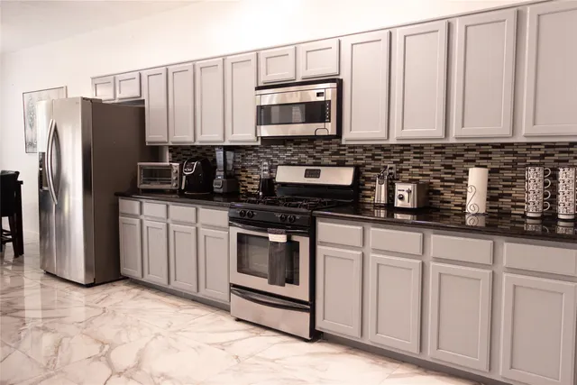 a kitchen with stainless steel appliances granite countertop a refrigerator a stove a sink and white cabinets