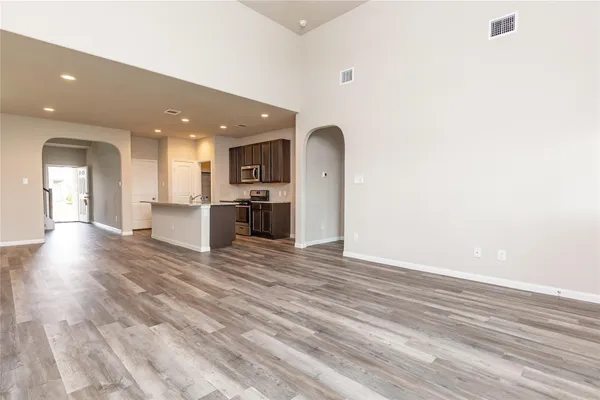 a view of empty room with wooden floor and kitchen view