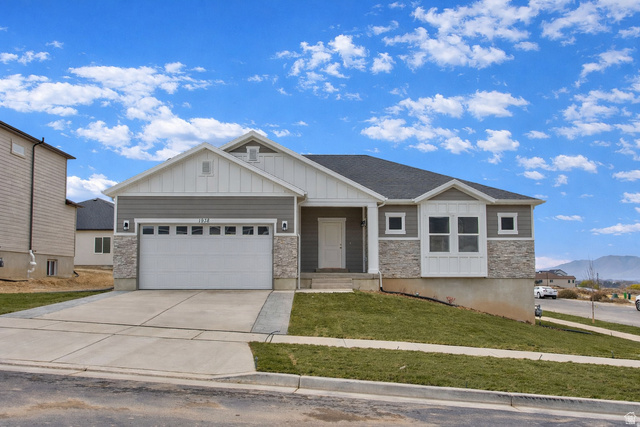 Craftsman house featuring board and batten siding, stone siding, a front lawn, and concrete driveway