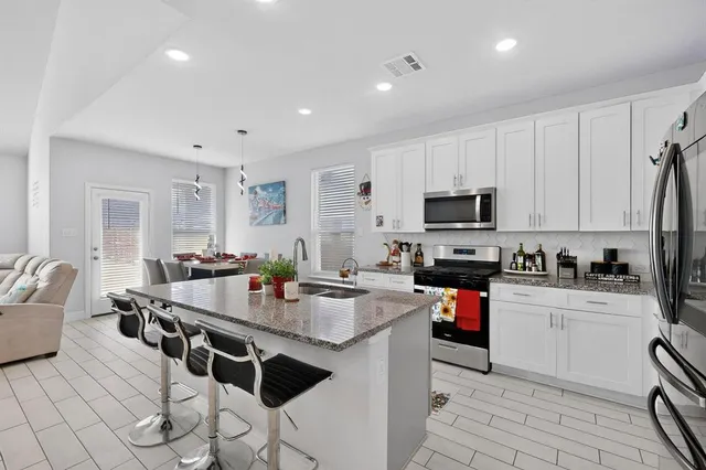 a kitchen with stainless steel appliances granite countertop a stove top oven a sink dishwasher and white cabinets with wooden floor