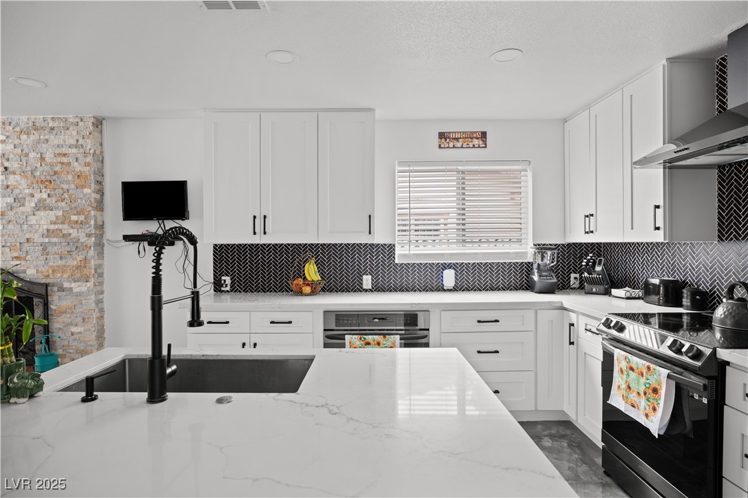 4231 Rimcrest Road Las Vegas, NV 89121 - Photo 12 of 52 Kitchen featuring appliances with stainless steel finishes, wall chimney range hood, white cabinets, tasteful backsplash, and recessed lighting