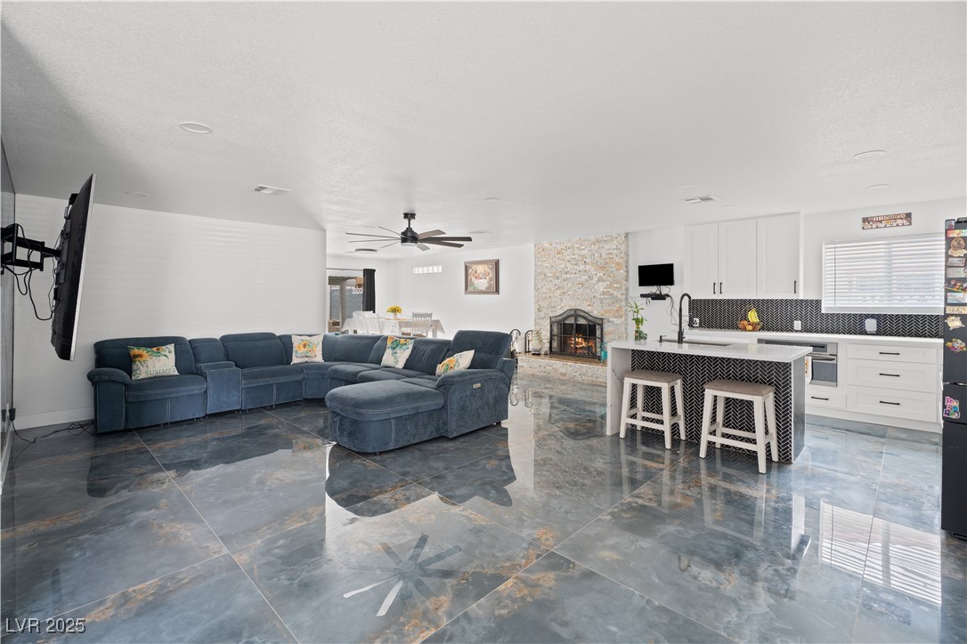 4231 Rimcrest Road Las Vegas, NV 89121 - Photo 10 of 52 Living room with healthy amount of natural light, ceiling fan, a stone fireplace, marble finish flooring, and a textured ceiling