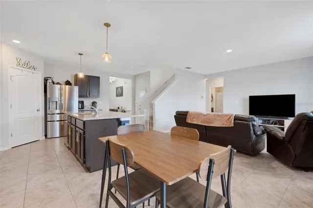 a kitchen with stainless steel appliances kitchen island granite countertop a dining table chairs and a refrigerator
