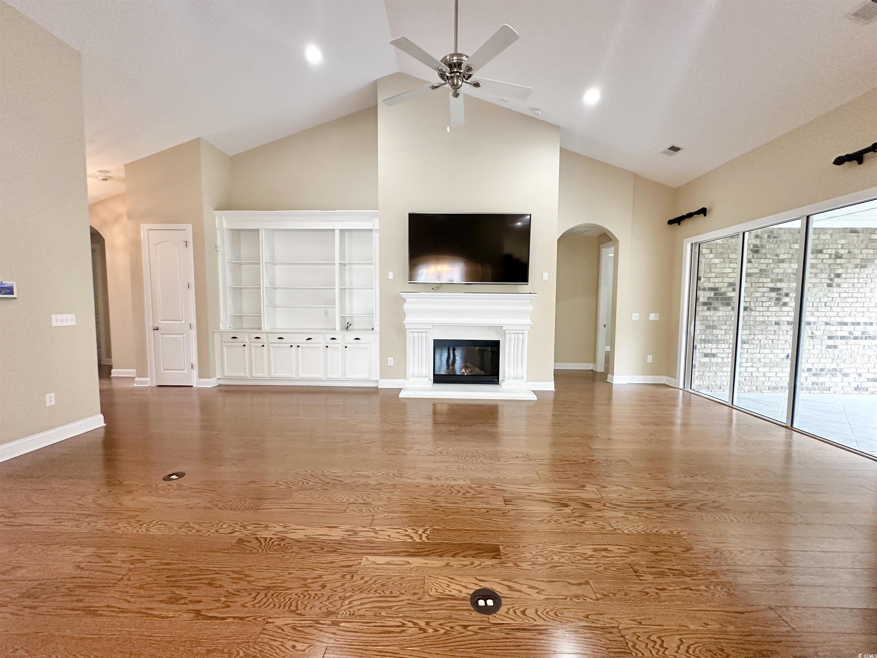 8472 Juxa Drive Myrtle Beach, SC 29579 - Photo 5 of 35 Unfurnished living room featuring arched walkways, a glass covered fireplace, high vaulted ceiling, wood finished floors, and a ceiling fan