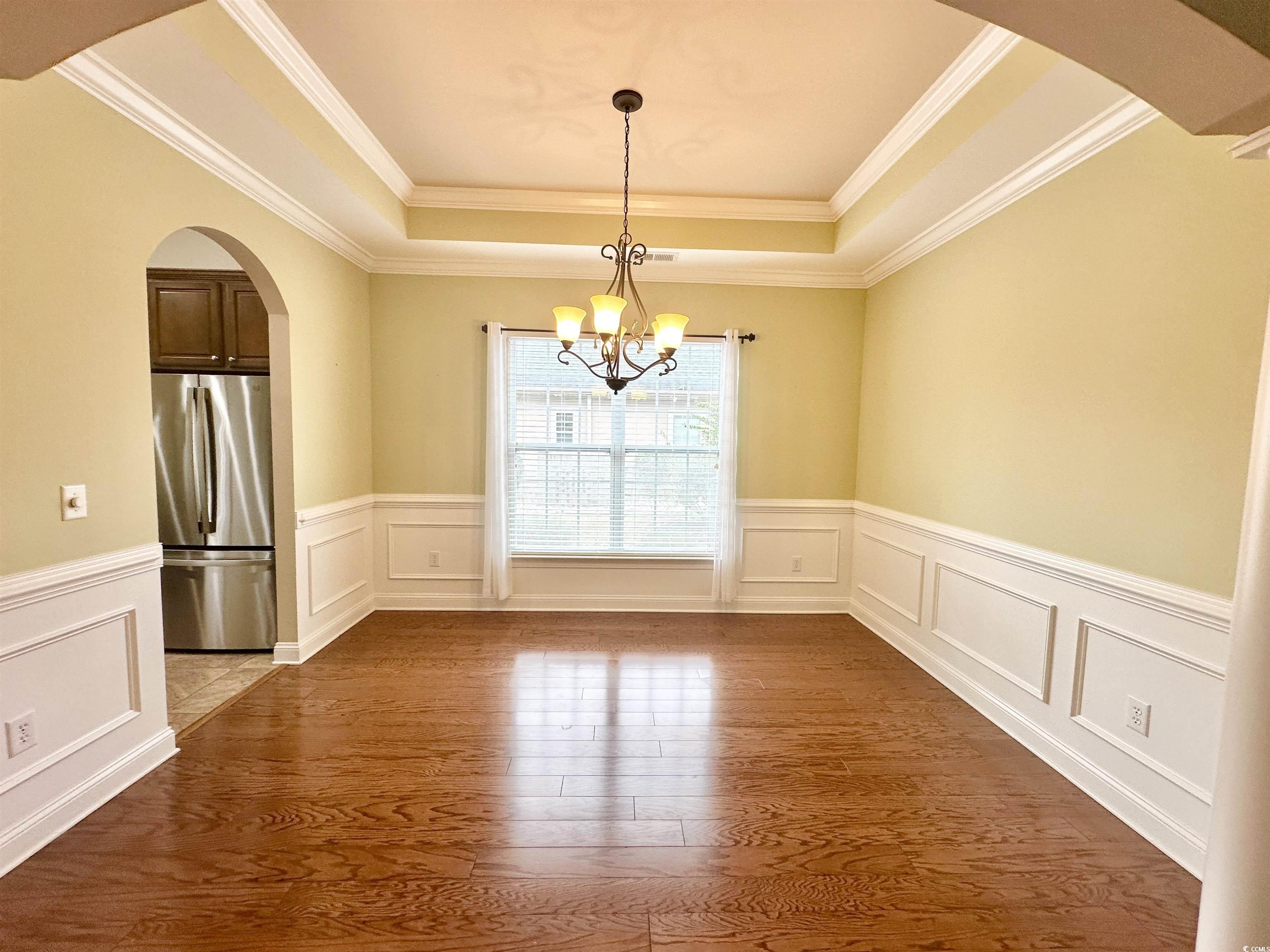 8472 Juxa Drive Myrtle Beach, SC 29579 - Photo 8 of 35 Unfurnished dining area featuring arched walkways, wood finished floors, crown molding, a wainscoted wall, and a chandelier