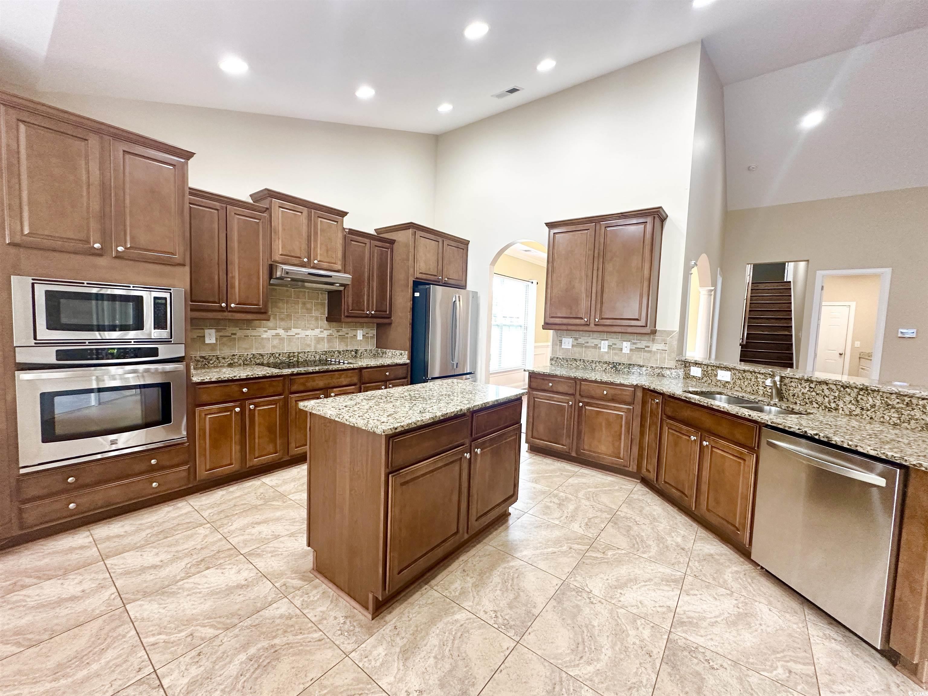 8472 Juxa Drive Myrtle Beach, SC 29579 - Photo 9 of 35 Kitchen with stainless steel appliances, a kitchen island, arched walkways, high vaulted ceiling, and light stone counters