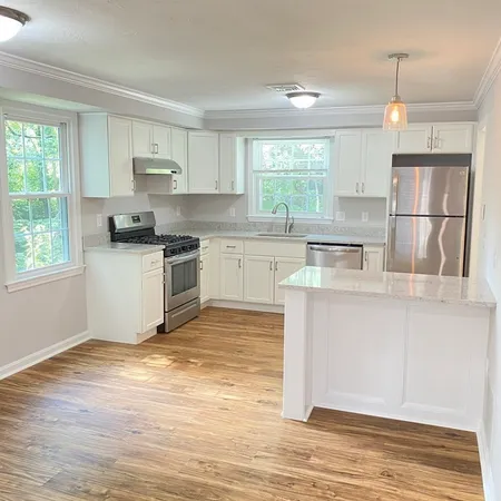 a kitchen with stainless steel appliances granite countertop a stove a sink dishwasher a refrigerator and white cabinets with wooden floor