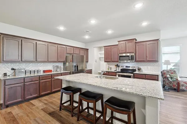 a kitchen with stainless steel appliances granite countertop a table chairs sink refrigerator and cabinets