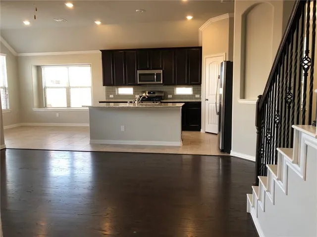 a kitchen with stainless steel appliances granite countertop a refrigerator a sink dishwasher a stove and a microwave oven on wooden floor