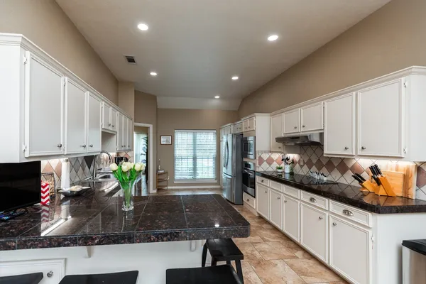 a kitchen with stainless steel appliances granite countertop a stove a sink a refrigerator white cabinets and wooden floor