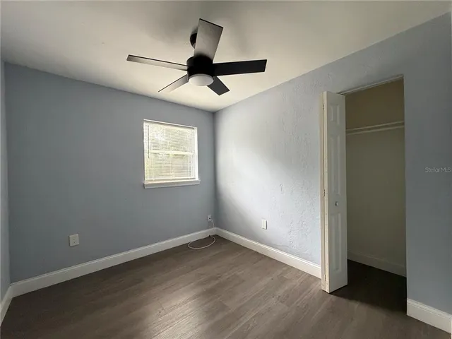 an empty room with wooden floor ceiling fan and windows