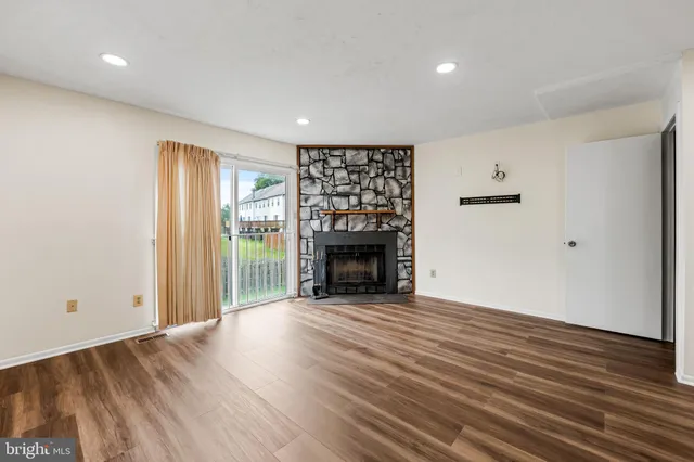 an empty room with wooden floor fireplace and windows