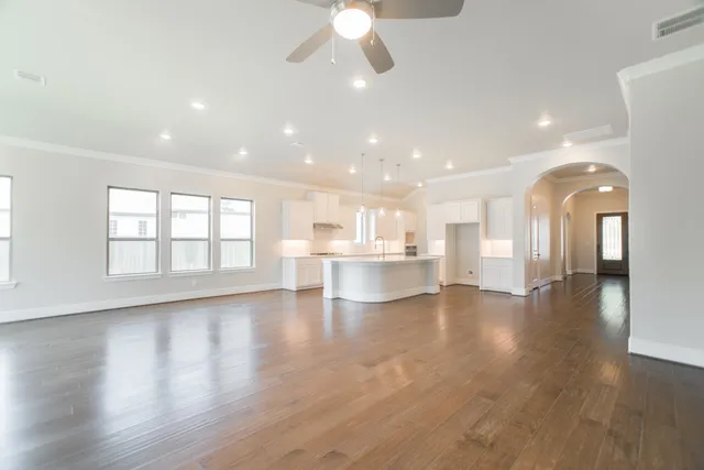 a view of an empty room with wooden floor and a kitchen