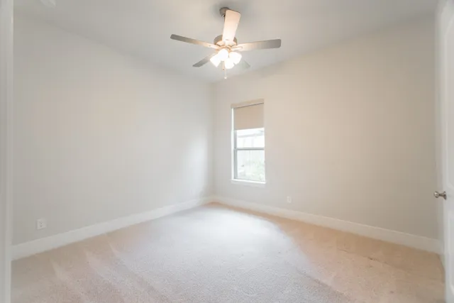 an empty room with a chandelier fan and windows