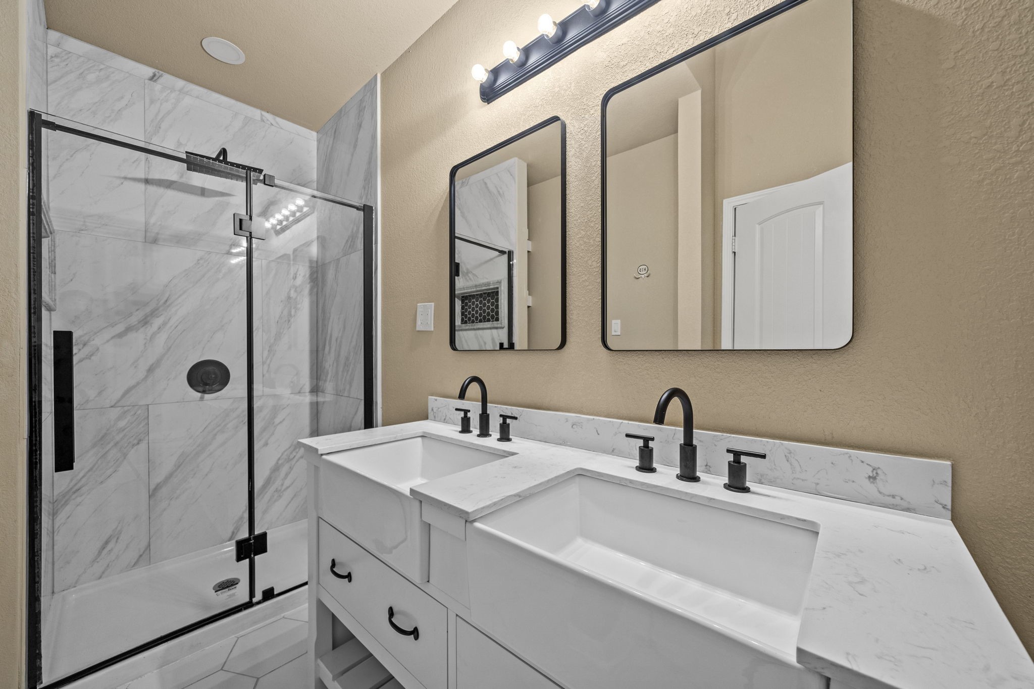 14215 Spindle Arbor Road Cypress, TX 77429 - Photo 24 of 47 This bathroom features a modern design with dual sinks, sleek black fixtures, and a spacious marble-tiled shower with a glass door. The vanity includes ample storage and contemporary mirrors, creating a stylish and functional space.