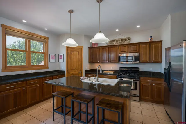 a kitchen with stainless steel appliances granite countertop a stove a sink a microwave a refrigerator and chairs