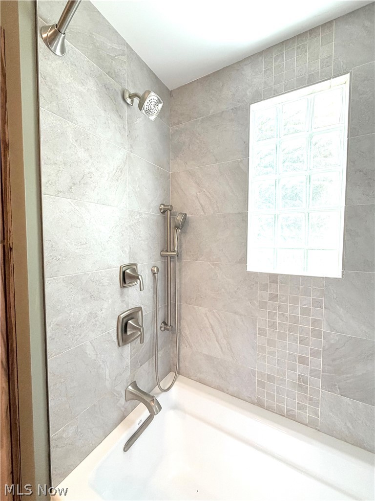 12590 Rockhaven Road Chesterland, OH 44026 - Photo 12 of 25 Bathtub with a large format gray tile surround, featuring a glass block window, brushed nickel fixtures, a rain shower head, and a handheld shower unit