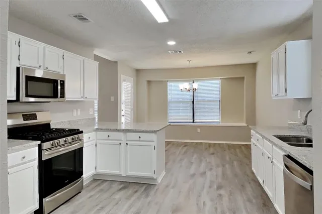 a kitchen with granite countertop a stove top oven a sink dishwasher and white cabinets with wooden floor