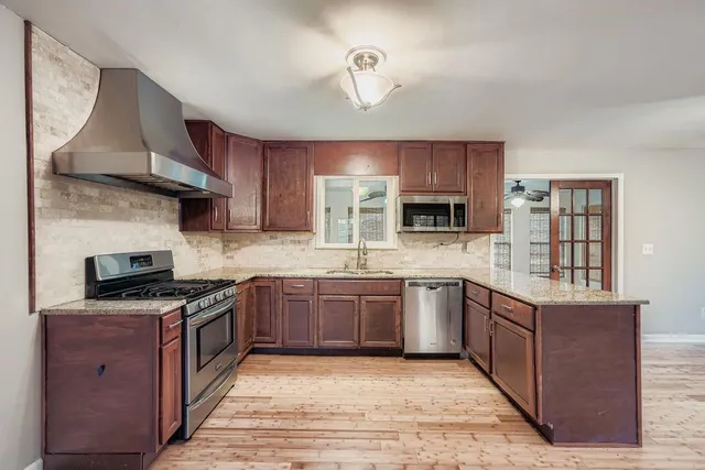 a kitchen with stainless steel appliances granite countertop wooden cabinets a sink dishwasher a stove and a refrigerator