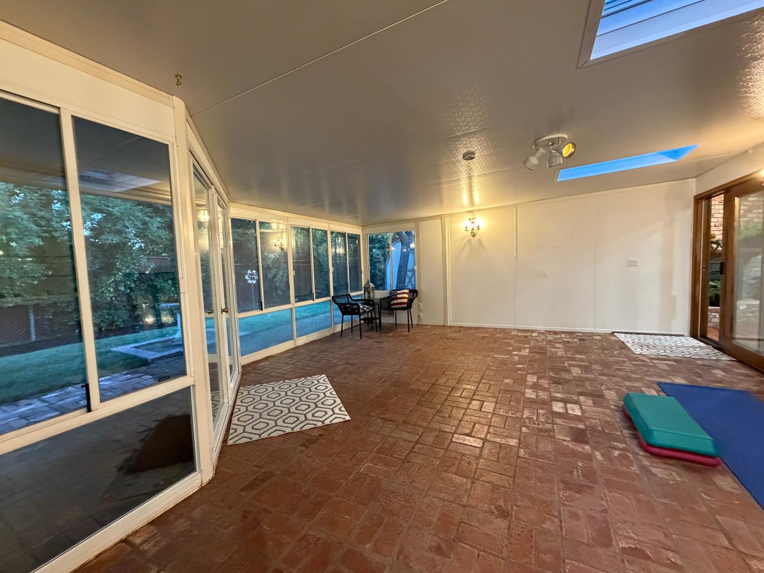 5706 Jeff Way Carmichael, CA 95608 - Photo 18 of 48 Sunroom at dusk, 2 skylights, and brick flooring with view of the park like backyard lined with plenty of shade from redwoods located along the elementary fence the home backs up to. New sod, D.G. and ground cover with updated irrigation system front and back.