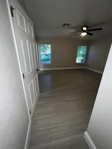 an empty room with wooden floor fan and windows