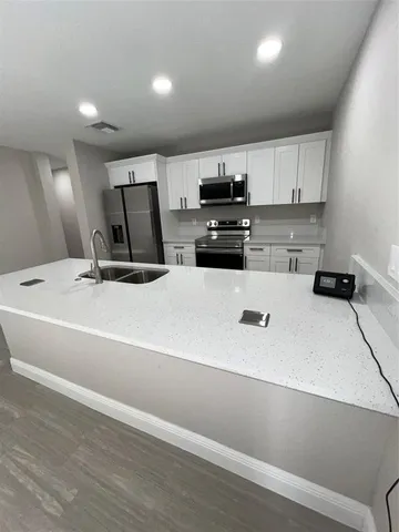 a kitchen with a sink stainless steel appliances wooden floor and view living room