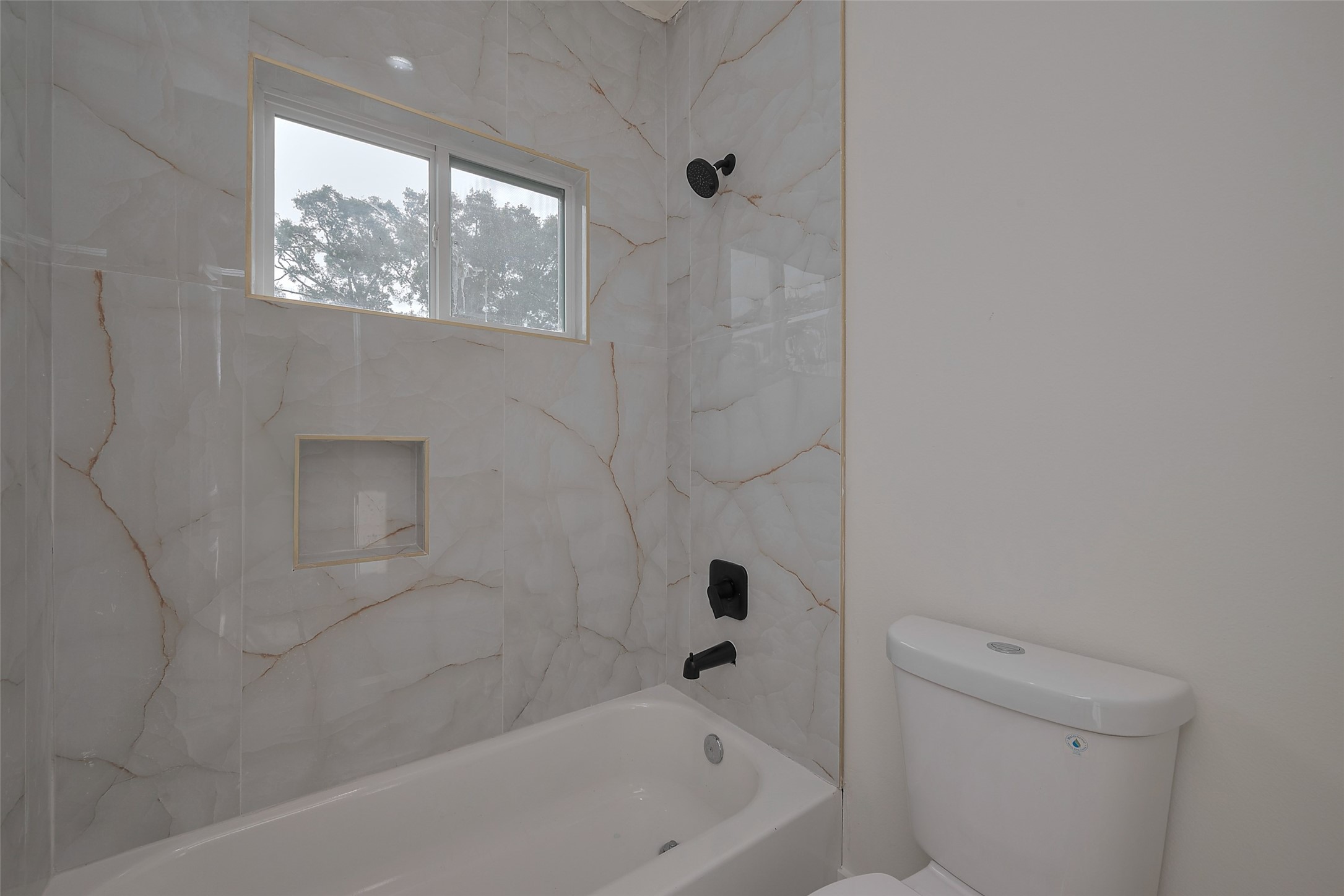 2422 Dalview Street Houston, TX 77091 - Photo 21 of 24 Enjoy spa-like vibes with this elegant
tub and shower combo, featuring
luxury floor-to-ceiling tile work and
matte black fixtures that bring out a
bold, contemporary touch.