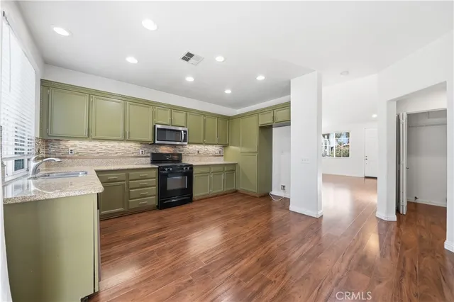 a kitchen with stainless steel appliances granite countertop a refrigerator oven a sink dishwasher and white cabinets with wooden floor