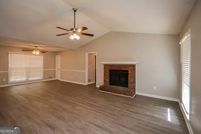 a view of an empty room with wooden floor fireplace and a window