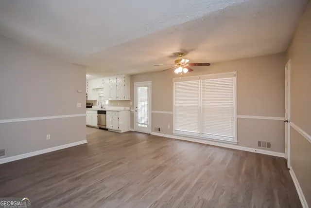 an empty room with wooden floor kitchen view and a window