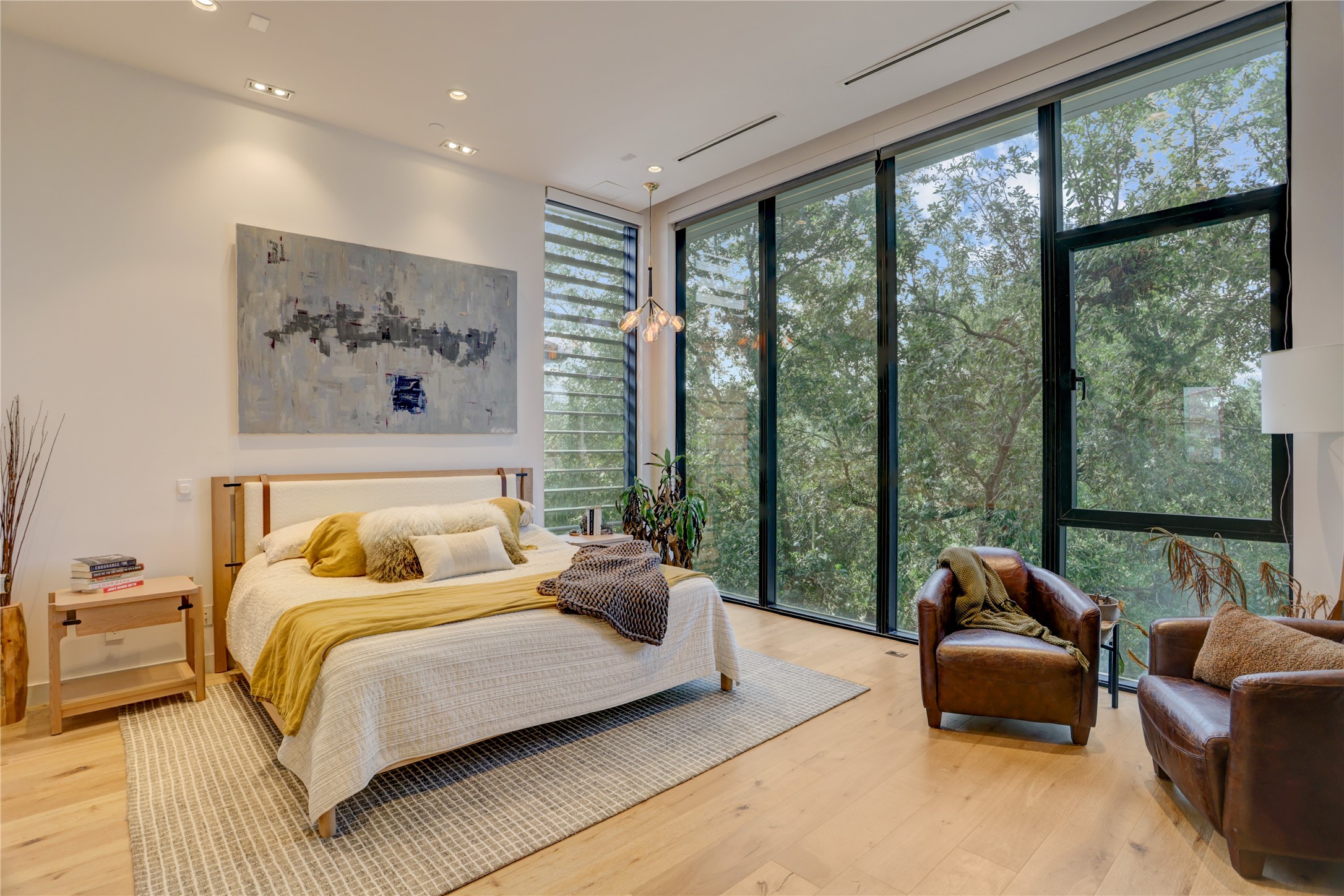 1807 Indiana Street Houston, TX 77006 - Photo 23 of 35 Primary Suite: Luxurious third-floor primary sanctuary showcasing a massive floor-to-ceiling glass wall with private treetop views, wide-plank wood flooring, recessed lighting, and ample space for a secondary sitting area.