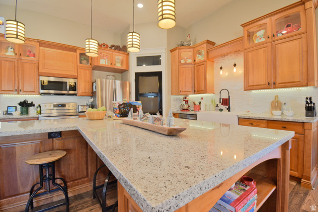 Kitchen featuring a breakfast bar area, glass insert cabinets, hanging light fixtures, stainless steel appliances, and light stone countertops