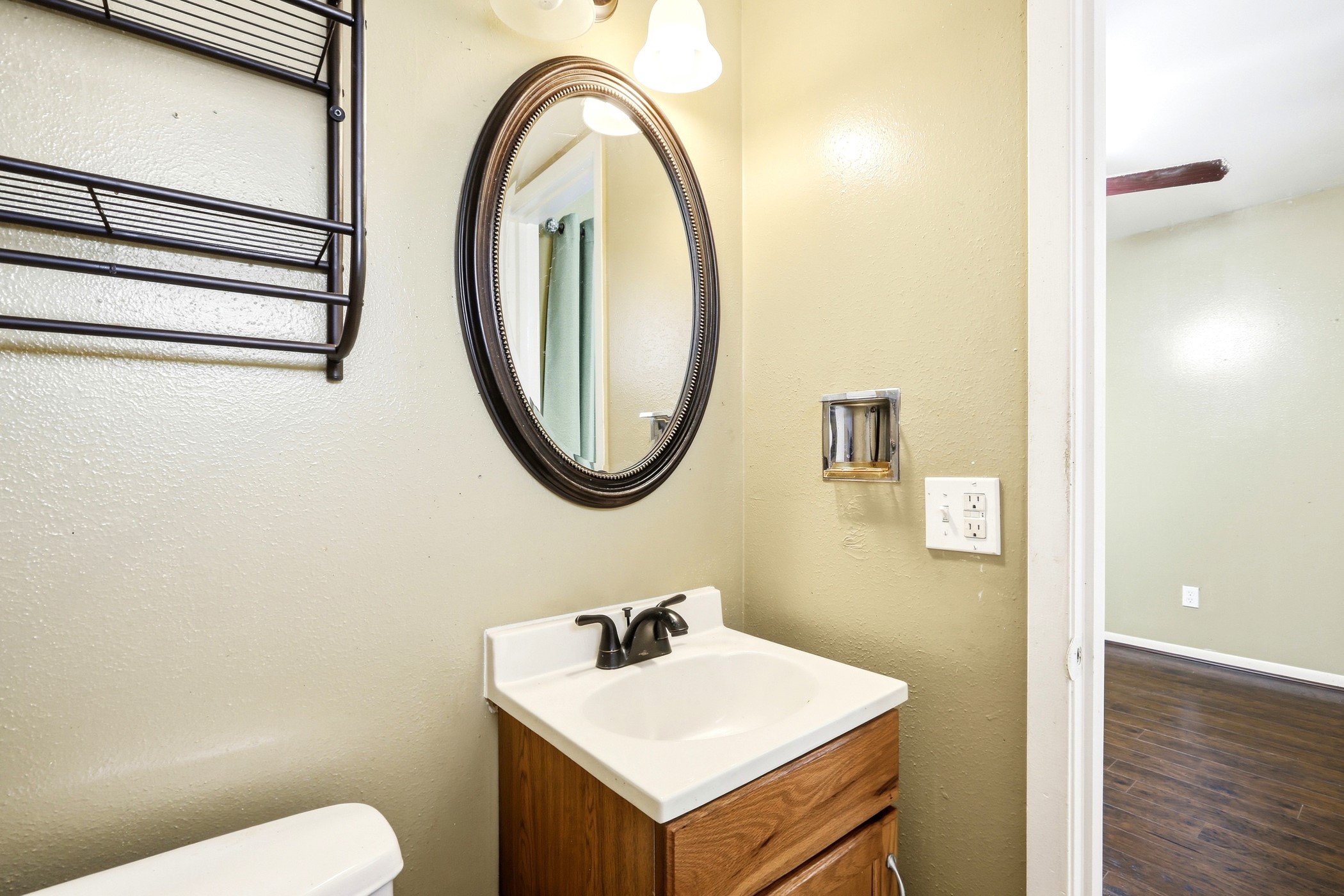 1507 Willow Rock Road Houston, TX 77088 - Photo 23 of 27 Half bath with a wood vanity, framed oval mirror, and wall-mounted shelf, convenient for guests.