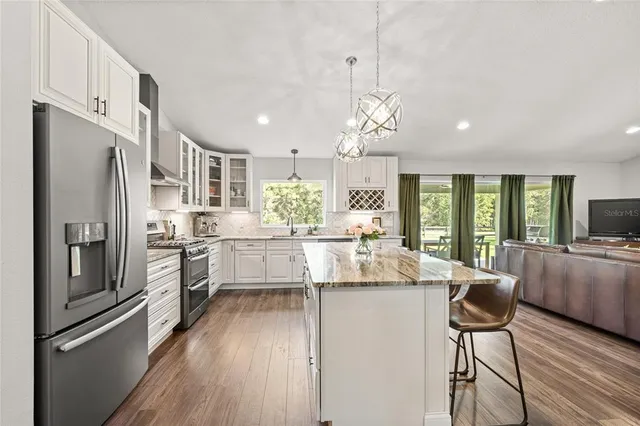 a kitchen with stainless steel appliances kitchen island granite countertop a refrigerator a stove a sink dishwasher a dining table and chairs with wooden floor