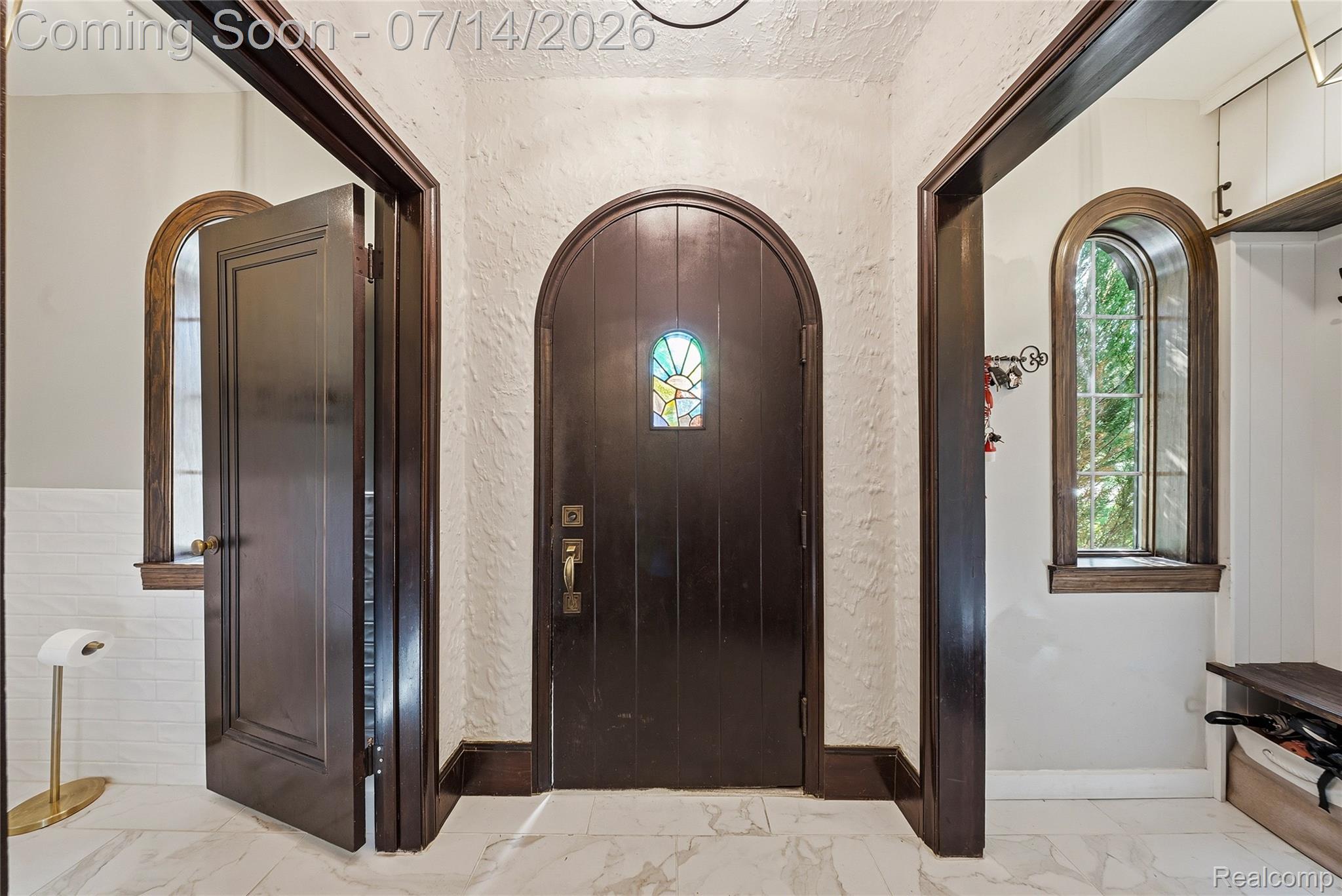 18460 Meridian Road Grosse Ile, MI 48138 - Photo 4 of 50 Arched entry door with stained glass detail, flanked by two arched windows, a built-in bench, and coat hooks