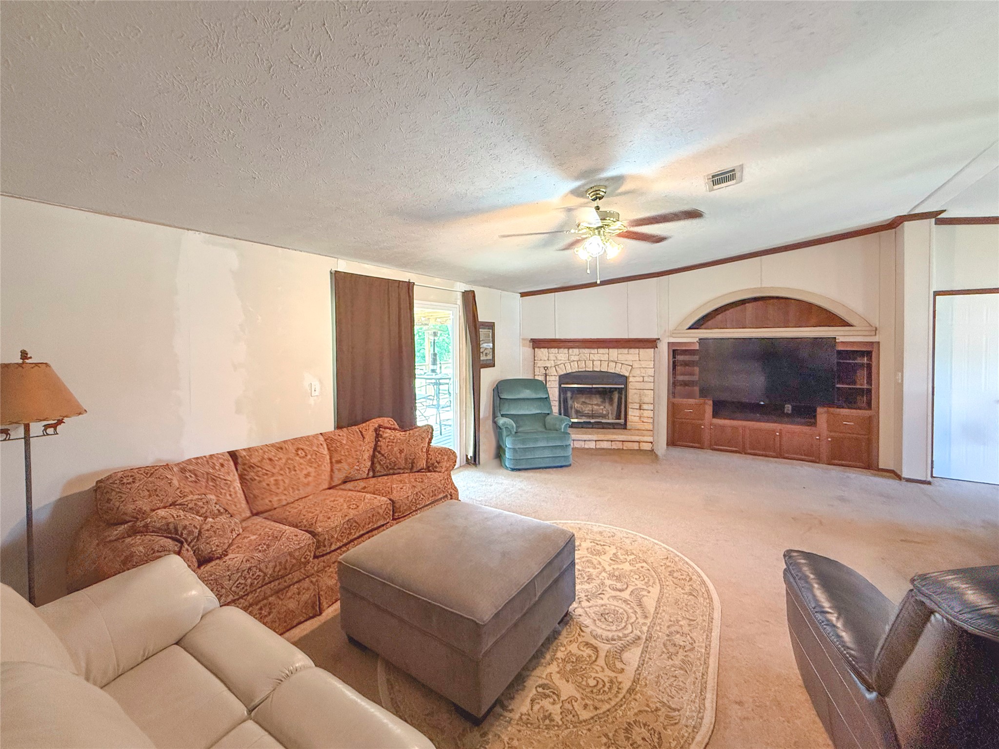 845 Caldwell Street Lexington, TX 78947 - Photo 6 of 39 Living room featuring ceiling fan, light colored carpet, a fireplace, a textured ceiling, and crown molding