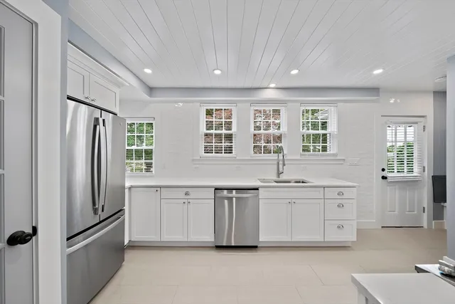 a large white kitchen with granite countertop a refrigerator and white cabinets