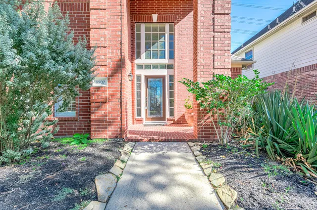 a view of a brick house with plants and large tree