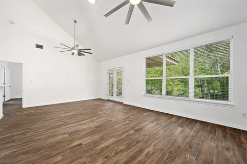 an empty room with wooden floor fan and windows