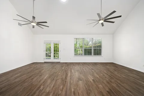 an empty room with wooden floor fan and windows