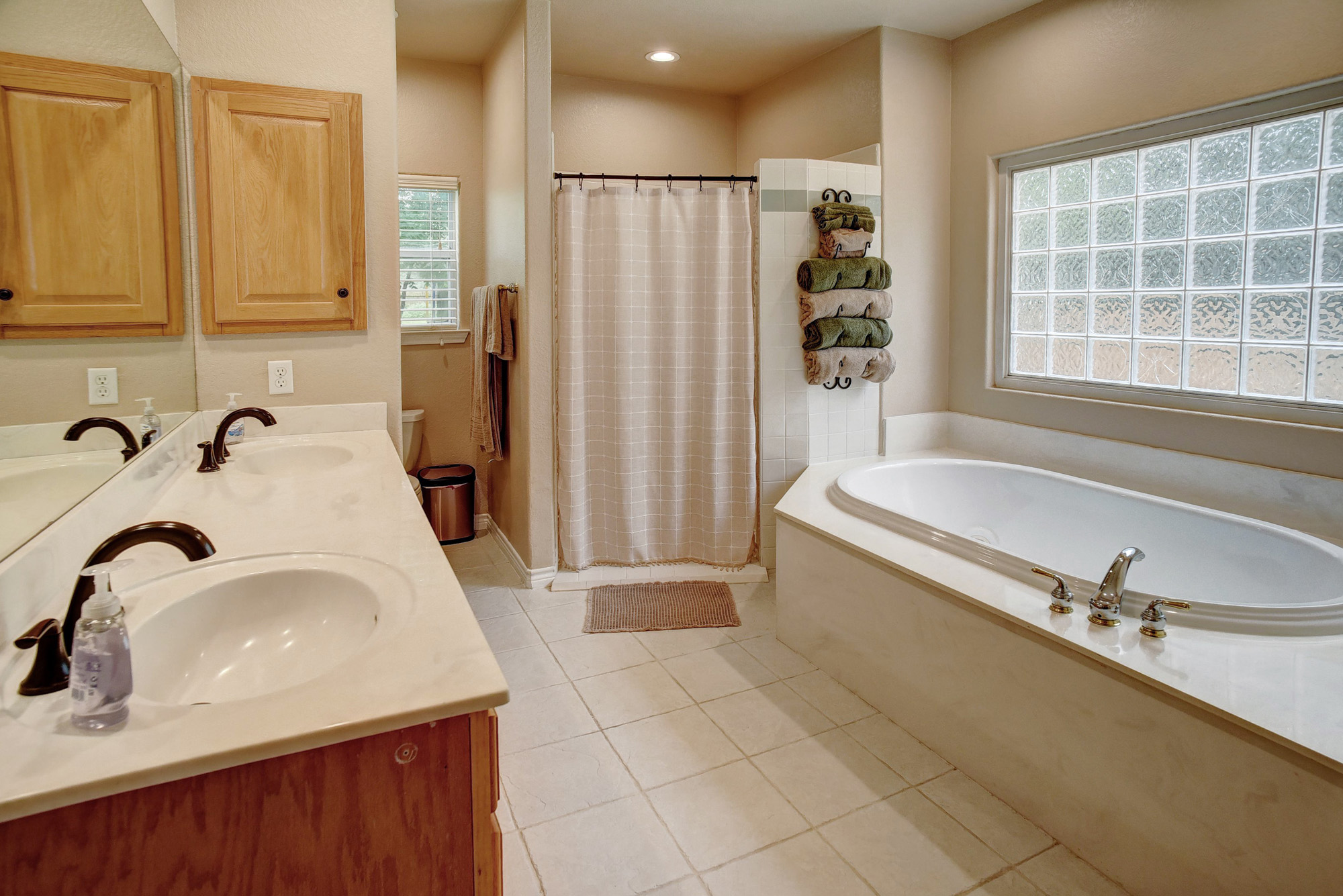 147 Spring Meadow Road Bastrop, TX 78602 - Photo 16 of 40 Bathroom featuring a built-in soaking tub with deck-mounted fixtures, a large glass block window, a double vanity with integrated sinks, wood-finish cabinetry, and tiled flooring