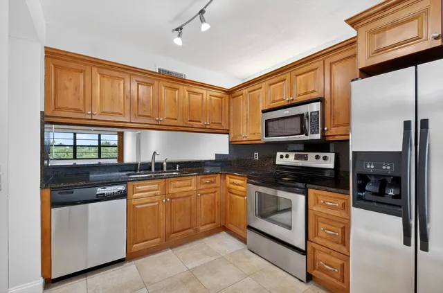 a kitchen with stainless steel appliances granite countertop a stove top oven a sink and dishwasher a refrigerator with wooden cabinets