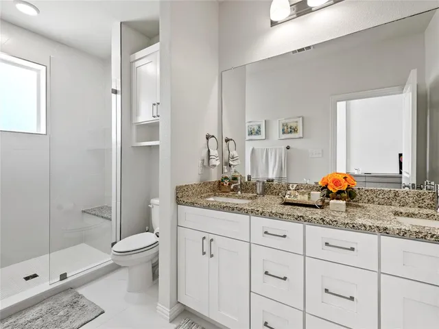 a bathroom with a granite countertop sink a toilet mirror and shower