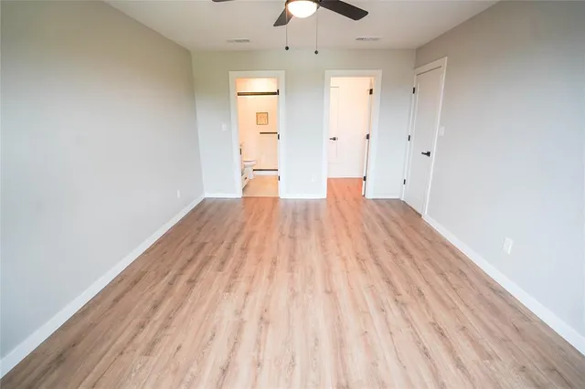 an empty room with wooden floor fan and windows