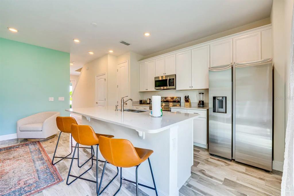 8209 Surf Street Kissimmee, FL 34747 - Photo 6 of 74 a kitchen with stainless steel appliances granite countertop a refrigerator a sink a stove a dining table and chairs with wooden floor