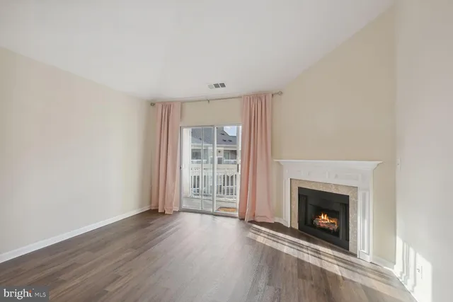 a view of an empty room with wooden floor fireplace and a window
