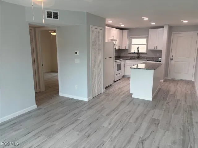 an empty room with wooden floor and way to kitchen